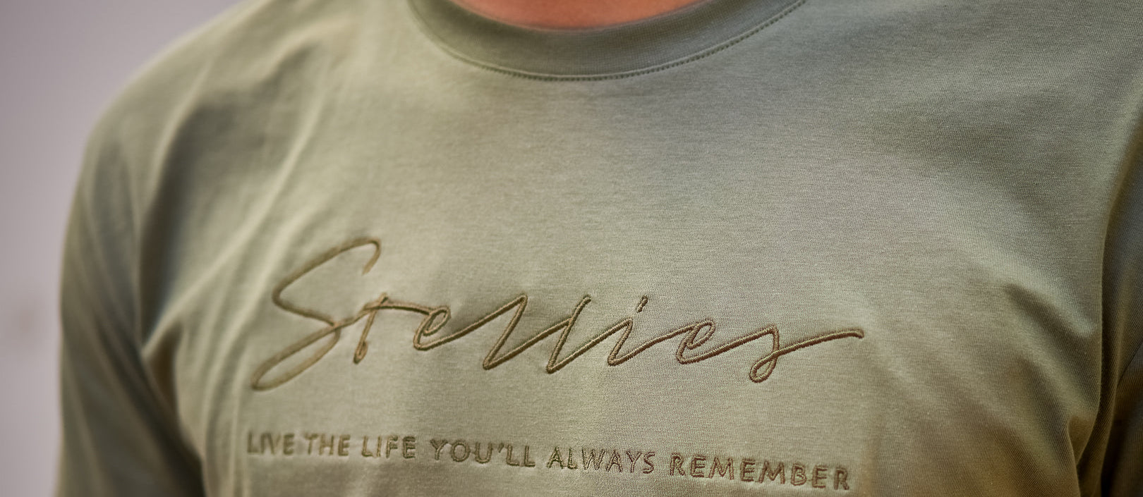 Green t-shirt with embroidered text on a plain background