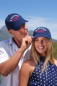 A man and a woman wearing navy blue caps with 'Stellenbosch' text on them, standing outdoors.